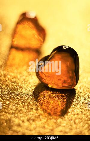 Bernsteinfarbene Glasherzen auf glitzerndem goldenen Tisch. Stockfoto