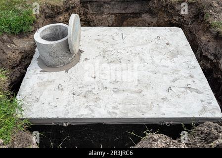 Klärbehälter aus Beton mit einem Fassungsvermögen von 10 Kubikmetern im Garten neben dem Haus, sichtbares Wasser darunter. Stockfoto