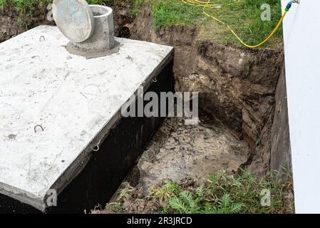 Klärbehälter aus Beton mit einem Fassungsvermögen von 10 Kubikmetern im Garten neben dem Haus, sichtbares Wasser darunter. Stockfoto