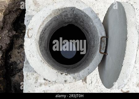 Klärbehälter aus Beton mit einem Fassungsvermögen von 10 Kubikmetern im Garten neben dem Haus, sichtbares Wasser darunter. Stockfoto