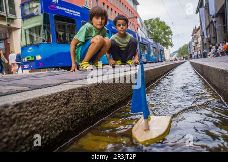 Niños jugando con un barquito de madera en los canales de agua, Münsterplattz, Friburgo de Brisgovia, Deutschland, Europa. Stockfoto