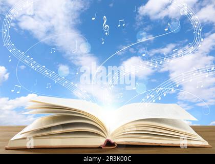 Musik aus dem Buch. Musiksymbole, die über dem Holztisch gegen den Himmel fliegen Stockfoto