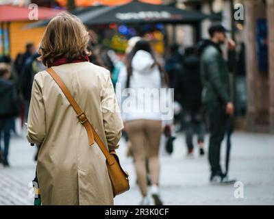 An einem regnerischen Frühlingstag spaziert eine unbekannte, modische Frau in Mode und Mantel durch eine urbane Straße und erkundet die Stadt. Stockfoto