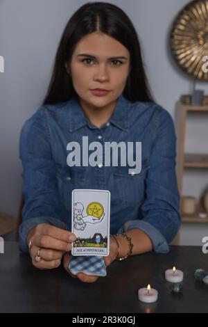 Wahrsager mit Tarotkarte Ace of Pentacles an grauem Tisch drinnen Stockfoto