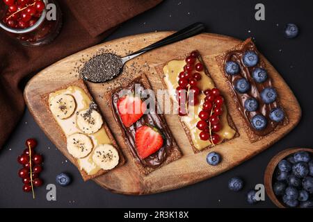 Frisches knuspriges Roggen-Knusperbrot mit verschiedenen Belägen auf einem schwarzen Tisch, flach liegend Stockfoto