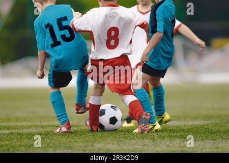 Eine anonyme Gruppe von Kindern im Grundalter spielt Fußball. Kinder laufen und treten einen Fußball. Jungs tragen blau-rote Sporttrikots Stockfoto