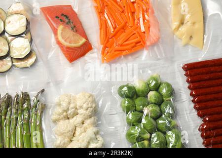 Verschiedene Lebensmittelprodukte in Vakuumverpackungen auf weißem Holztisch, flach liegend Stockfoto