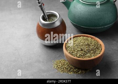 Calabash mit Bombilla, Teekanne und Schüssel Teeblätter auf grauem Tisch, Platz für Text Stockfoto