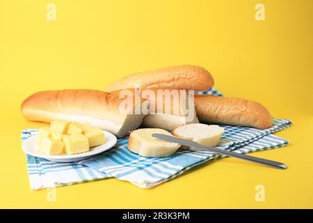 Ganze und geschnittene Baguettes mit frischer Butter auf gelbem Hintergrund Stockfoto