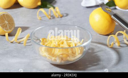 Schüssel mit Schälteilen, frischen Zitronen und Zester auf grauem Tisch Stockfoto