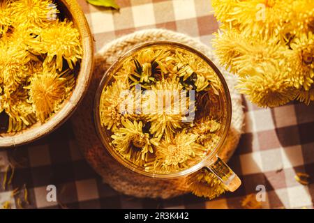 Löwenzahnblüte gesunder Tee im Glasbecher auf dem Tisch. Kräutermedizin köstlicher Tisane-Tee mit frischem gelben Blütendandelio Stockfoto