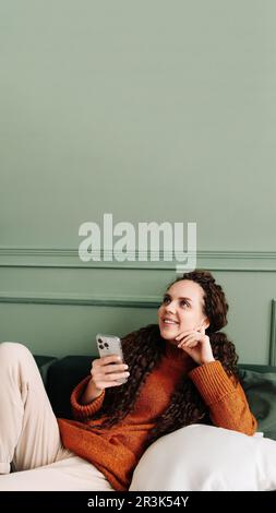 Glückliche junge Frau, die ein Mobiltelefon für E-Commerce-Shopping und -Unterhaltung zu Hause nutzt. Fröhliche Frau, die Online-Unterhaltung auf Smartphone bei genießt Stockfoto