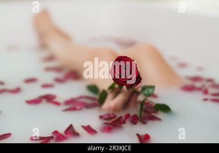 Die Frau entspannt sich in einem Bad mit Milch und Rosenblättern. Stockfoto