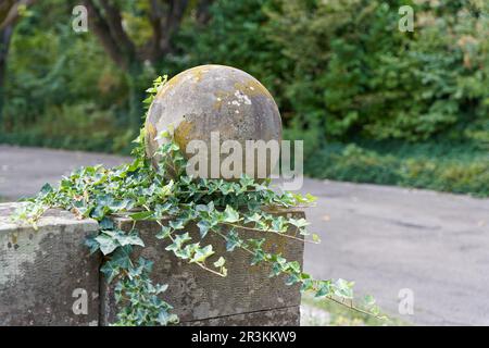 Kolonne mit Kugel überwuchert mit Efeu als Dekoration auf einem Pfad in einem öffentlichen Park Stockfoto