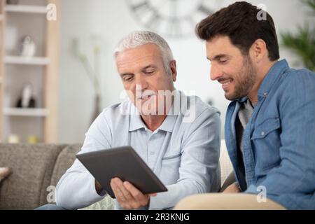 Erwachsener Sohn, der einem älteren Vater das Tablet beibringt Stockfoto