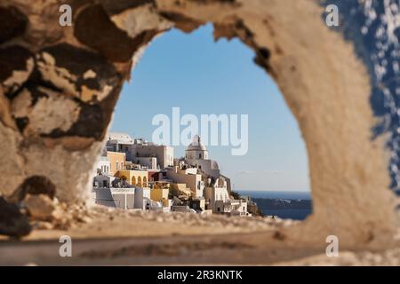 Gerahmter Blick zwischen einer kleinen blauen Kuppel - Fira Village auf Santorini Island, Griechenland - traditionelle weiße Häuser in der Caldera Cliff Stockfoto