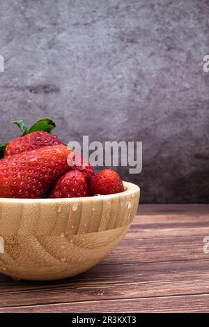Süße, frisch gewaschene rote Erdbeeren in einer Holzschüssel auf einem Tisch. Vertikales Bild mit selektivem Fokus, Wassertropfen als Detail. Stockfoto