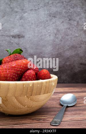 Süße, frisch gewaschene rote Erdbeeren in einer Holzschüssel auf einem Tisch. Vertikales Bild mit selektivem Fokus, Wassertropfen als Detail. Stockfoto