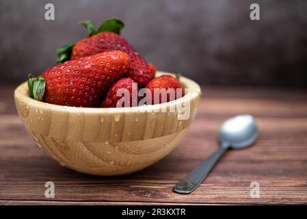 Süße, frisch gewaschene rote Erdbeeren in einer Holzschüssel auf einem Tisch. Selektiver Fokus, Wassertropfen. Stockfoto