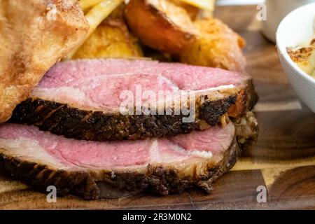 Eine Nahaufnahme von dicken Scheiben frisch gekochtem, mittlerem, seltenem Rinderstriploin, serviert als Teil eines englischen Roastdinner. Das Fleischfett wird gebraten Stockfoto