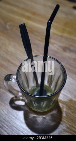 Metalllöffel und Plastikstroh in einem leeren Glas in einem Café. Stockfoto