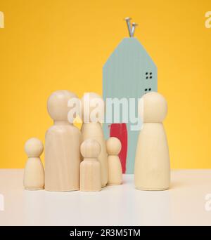 Holzhaus und Miniaturfiguren einer Familie und eines maklers auf gelbem Hintergrund. Stockfoto