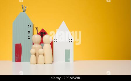 Holzhaus und Miniaturfiguren einer Familie auf gelbem Hintergrund. Das Konzept des Verkaufs und Kaufs von Immobilien Stockfoto