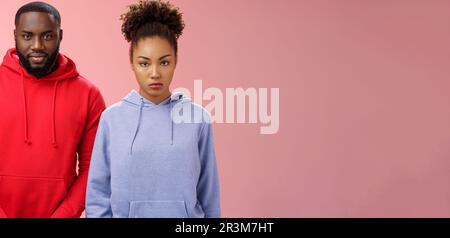 Zwei süße afroamerikanische Geschwister stehen zusammen, rosa Hintergrund, zum Familienessen eingeladen, neue mom, Freund, Schwester Look Stockfoto