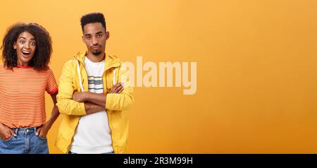 Zwei afroamerikanische Freunde stehen über orangefarbenem Hintergrund, Mädchen denkt Idee ist genial Gefühl aufgeregt und fröhlich, während boyfr Stockfoto