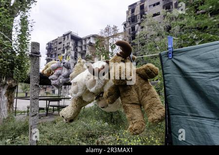 Kinderspielzeug hängt an einem Seil vor dem Hintergrund von zerstörten verbrannten Häusern in der Ukraine Stockfoto