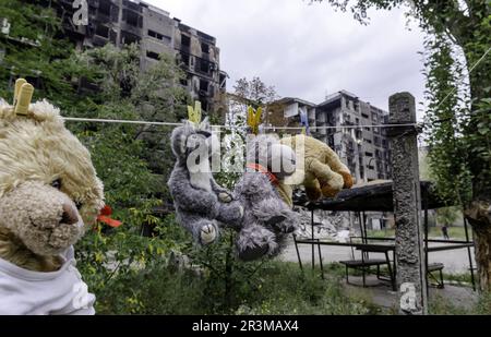 Kinderspielzeug hängt an einem Seil vor dem Hintergrund von zerstörten verbrannten Häusern in der Ukraine Stockfoto