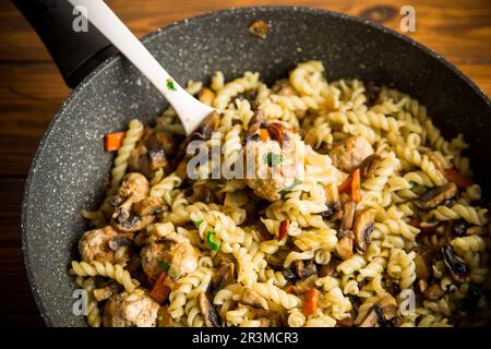 Vermicelli mit Pilzen, Fleisch und Gemüse in einer Bratpfanne auf einem Holztisch gekocht Stockfoto