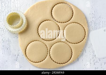 Das Schneiden von Hüttenkäsekeksen mit Schimmelpilzen aus Weichteig, der auf einem Brett gerollt wird. Köstliche hausgemachte Kuchen Stockfoto