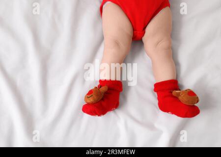 Baby trägt festliche Weihnachtssocken auf weißem Bettlaken, Draufsicht Stockfoto