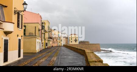 Blick auf die historische Uferpromenade mit befestigten Mauern und Verteidigungsanlagen in Alghero unter stürmischem, bewölktem Himmel Stockfoto