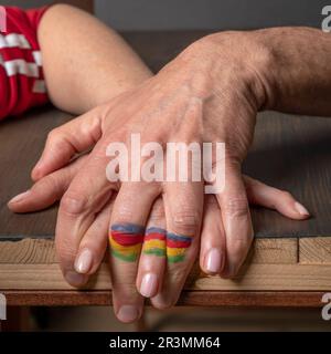 Eine weibliche Hand ist mit einer männlichen Hand verbunden und bildet eine farbige Fahne an den Fingern Stockfoto