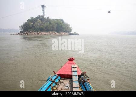 Traditionelles hölzernes Passagierboot auf einem Brahmaputra Fluss in der Nähe von Guwahati mit Flussinsel und Seilbahn hinten an einem nebeligen Sommertag in Assam, Indien Stockfoto