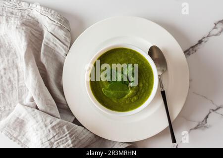 Gesundes Frühstück, grüner Brokkoli und Spinatcremesuppe in einer weißen Schüssel auf Marmorhintergrund mit grauer Serviette, Draufsicht Stockfoto