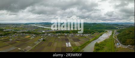 Panoramablick aus der Vogelperspektive auf den Fluss, der sich an bewölkten Tagen um Reisfelder in ländlicher Landschaft schlängelt Stockfoto