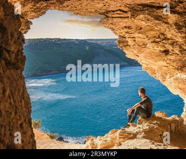 Gozo Insel Malta, junger Mann in einer Höhle mit Blick auf den Ozean Stockfoto