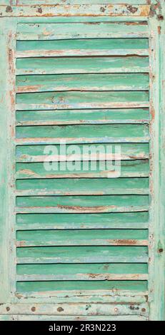 Eine alte Fenstertür aus Holz mit horizontalen Leisten ist mit abblätternder grüner Farbe lackiert. Vertikales Bild. Stockfoto