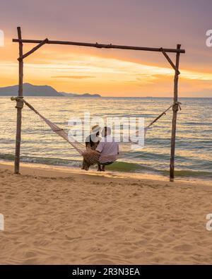Männer und Frauen beobachten den Sonnenuntergang von einer Hängematte am Strand in Pattaya Thailand Ban Amphur Beach Stockfoto