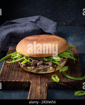 Chilenischer lateinamerikanischer Sandwich-Burger Chacarero mit hochwertigen Rinderschnitten und grünen Bohnen auf schwarzem Hintergrund. Stockfoto