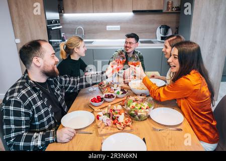 Eine Gruppe von Freunden versammelte sich an einem schönen Tag, um Zeit miteinander zu verbringen, zu essen und zu lachen. Toasten mit einem Glas Apperol. Hochwertiges Foto. Stockfoto