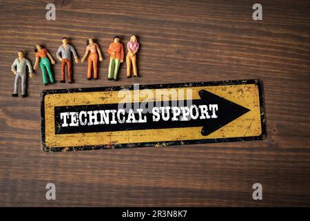 Technischer Support. Richtungspfeil und kleine menschliche Figuren auf einem hölzernen Hintergrund. Stockfoto