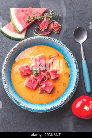 Salmorejo-Suppe mit Wassermelone. Traditionelle spanische kalte Tomatensuppe mit Wassermelone und serrano-Schinken auf blauem Teller, Schieferteller Stockfoto