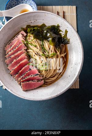 Thunfischsteak Ramen. Japanische Suppe mit Nudeln Ramen, Miso, gebratenem Thunfischsteak und Algen aus Algen. Draufsicht. Blauer Hintergrund. Stockfoto