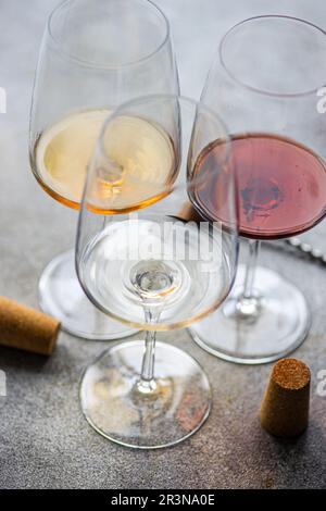 Hoher Winkel von drei Hauptsorten georgischer Trockenweine - weiß, rot und bernsteinfarben auf einem betongrauen Tisch mit einem Korkenzieher und Korken Stockfoto