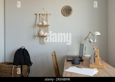 Innenausstattung des minimalistischen Zimmers mit Studententasche und Holztisch mit Stuhl und Laptop in Fensternähe im modernen Apartment Stockfoto