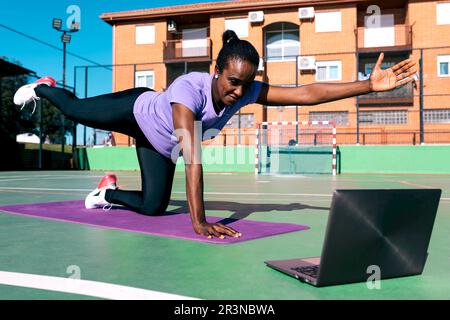 Ein ganzer Körper aus motivierten jungen, schwarzen, weiblichen Sportlerinnen in Activewear, die mit angehobenen Armen am Boden Kickback-Training mit Klebstoff machen und dabei Online-Fitness anschauen Stockfoto